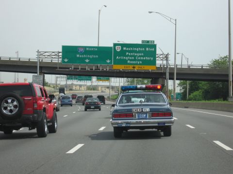 1991 Ford LTD Crown Victoria - dark blue Chevrolet Caprice with a lightbar shares a highway lane with a red Hummer beneath an I-395 North overhead sign.