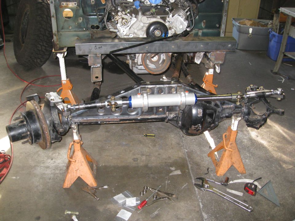 Jeep YJ axle assembly with steering damper on jack stands in workshop.