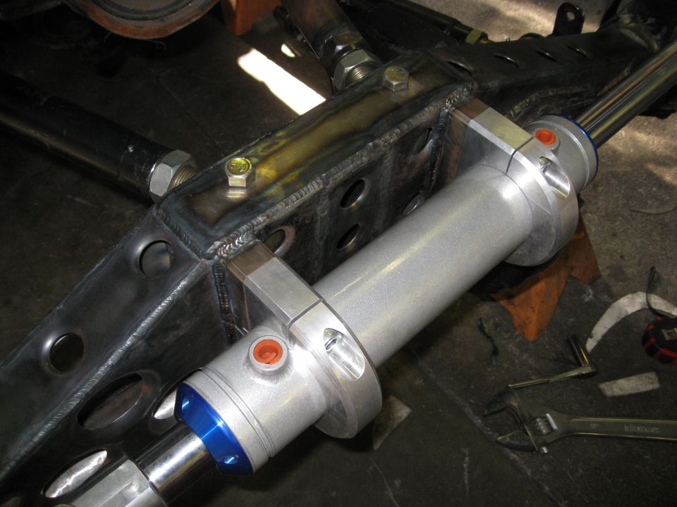Silver steering stabilizer cylinder mounted to a Jeep YJ frame with tools on the floor.