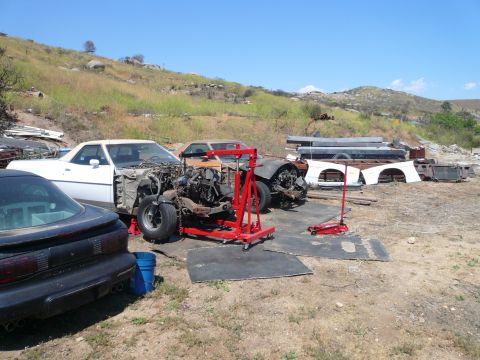 1975 Ford Ranchero - A white Ford Ranchero is parked in an outdoor lot with its engine removed and supported by an engine hoist. A black Pontiac Firebird is par…