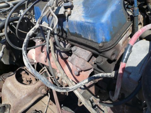 1975 Ford Ranchero - A close-up view of a V8 engine with a blue valve cover and rusted exhaust manifold. Various hoses and wiring are visible throughout the eng…