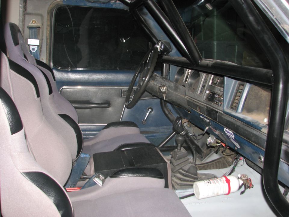 Interior of a modified vehicle with racing seats, roll cage, and fire extinguisher.