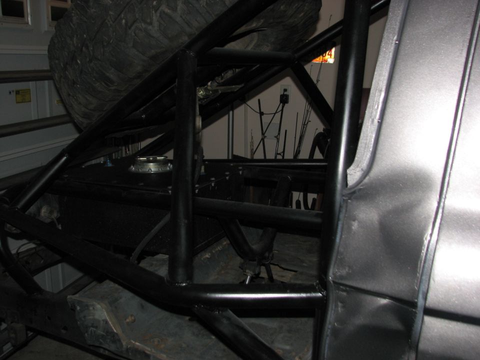 Interior rear view of a custom off-road vehicle with roll cage, tire, and fuel tank.
