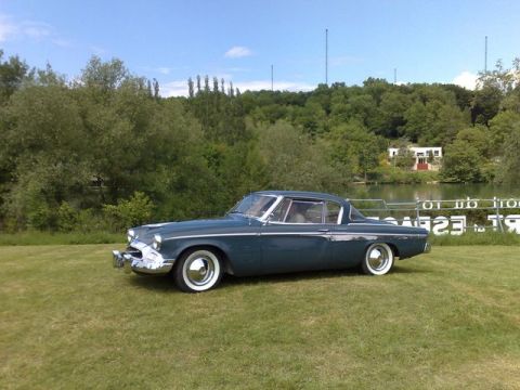 1991 Ford Crown Victoria - A blue 1955 Studebaker coupe is parked on a grassy area next to a lake under a clear sky.