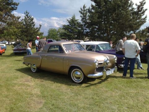 1991 Ford Crown Victoria - A vintage gold coupe is displayed at an outdoor car show with other vehicles and people around.