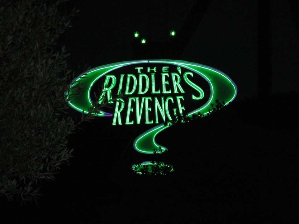 Neon green sign that reads "THE RIDDLER'S REVENGE" shaped like a question mark.