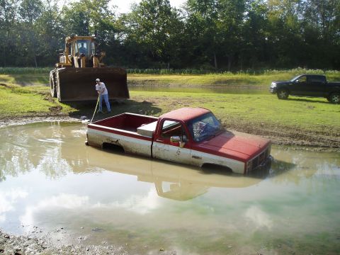 1995 Mercury Grand Marquis - A red and white pickup truck is stuck in a muddy body of water, with a bulldozer visible in the background.