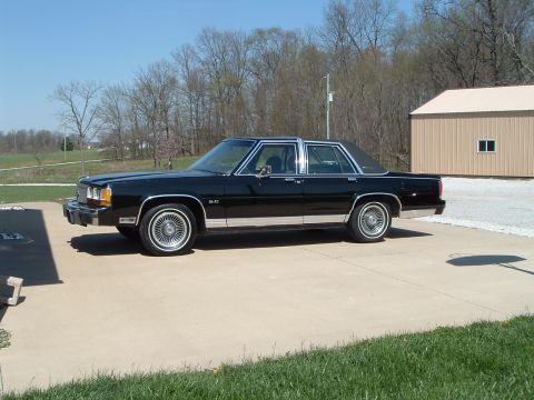 1989 Ford Crown Victoria LTD - A black sedan with chrome accents and a vinyl roof is parked on a concrete driveway.