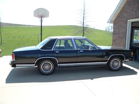 1989 Ford Crown Victoria LTD - Side view of a black 1989 Ford Crown Victoria LTD parked in front of a brick garage.