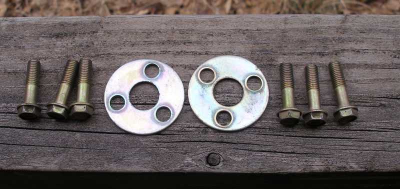 Six zinc-plated flange bolts and two three-hole cam gear retainer plates on wood plank