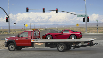 1991 Ford Crown Victoria - A red sports car is loaded onto a tow truck on a highway with traffic lights in the background.