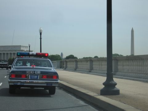 1991 Ford LTD Crown Victoria - black-and-white Chevrolet Caprice police cruiser drives a bridge lined with lamp posts, the Washington Monument and Lincoln Memorial visibl…