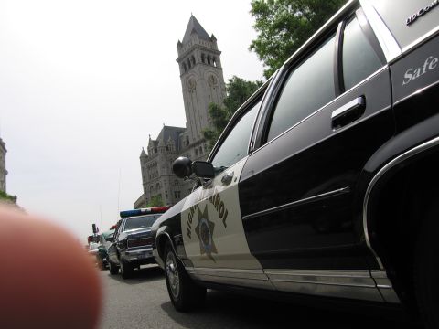 1991 Ford LTD Crown Victoria - low-angle shot of a black-and-white Highway Patrol sedan with a fingertip in frame, the Old Post Office clock tower rising behind.