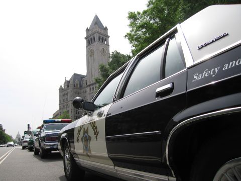 1991 Ford LTD Crown Victoria - Side profile of a black-and-white Highway Patrol Ford Crown Victoria cruiser parked along a street with the Old Post Office clock tower in…