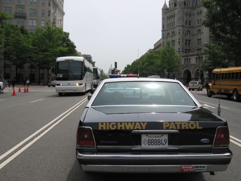 1991 Ford LTD Crown Victoria - Rear view of a black Ford Crown Victoria marked HIGHWAY PATROL with a California plate, parked on a city street near a tour bus and school…