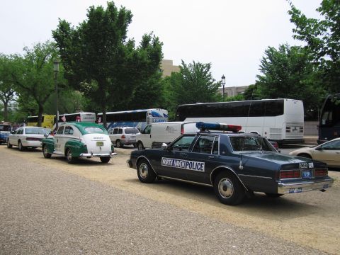 1991 Ford LTD Crown Victoria - North Haven Police Chevrolet Caprice and older sheriff and classic cars are parked on a gravel lot with tour buses and trees behind.