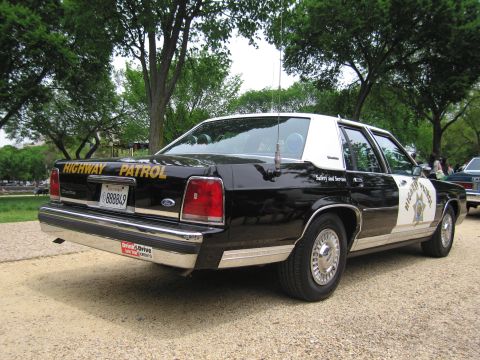 1991 Ford LTD Crown Victoria - Rear three-quarter view of a black-and-white Highway Patrol Ford sedan marked Safety and Service, parked on gravel with a dealer plate fram…