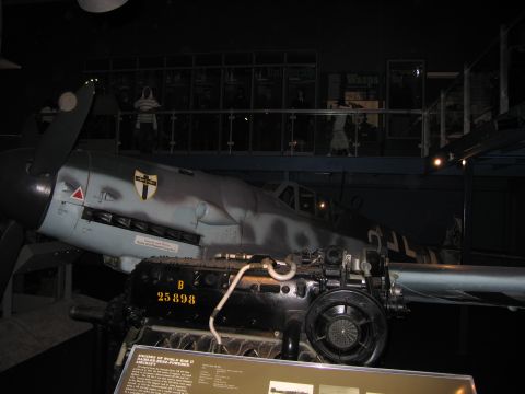 1991 Ford LTD Crown Victoria - gray fighter aircraft fuselage with shield emblem on museum display behind an inline aircraft engine marked B 25898.