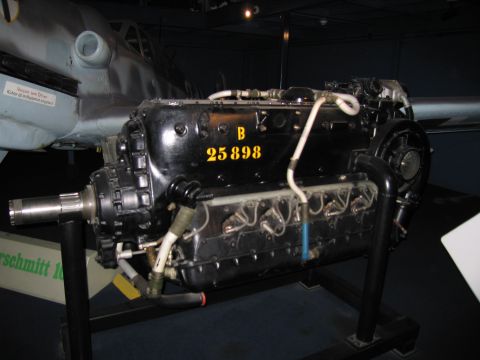 1991 Ford LTD Crown Victoria - black inverted-V inline aircraft engine marked B 25898 on a stand beside a gray fighter aircraft in a museum display.