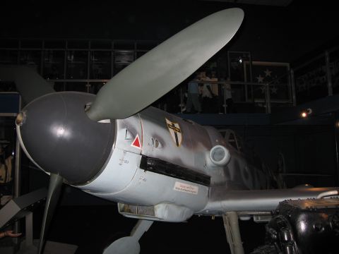 1991 Ford LTD Crown Victoria - nose, spinner, and propeller of a gray German fighter aircraft with shield emblem, displayed in a dimly lit museum hall.