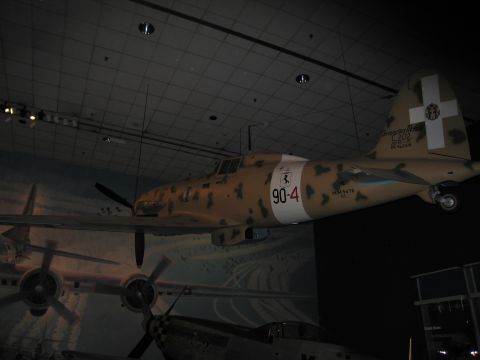 1991 Ford LTD Crown Victoria - tan desert-camouflage fighter aircraft marked 90-4 with white cross tail suspended over a mural in a dim museum hall.
