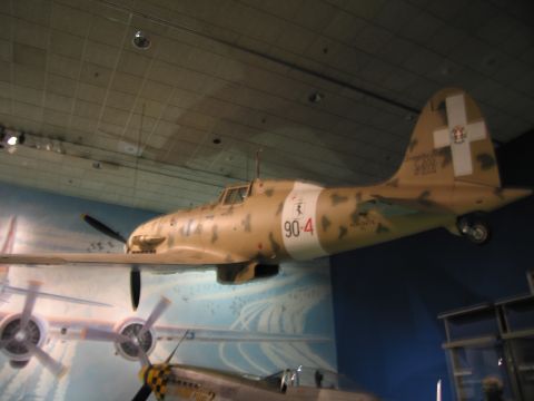 1991 Ford LTD Crown Victoria - tan desert-camouflage fighter aircraft marked 90-4 with white cross on the tail, displayed above a mural in a museum hall.