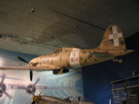 1991 Ford LTD Crown Victoria - tan desert-camouflage fighter aircraft marked 90-4 with white tail cross suspended over a painted mural in a museum hall.