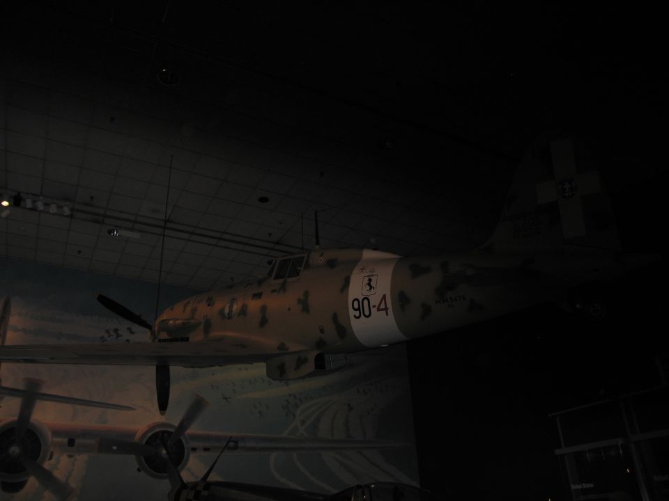 Tan camouflage fighter aircraft marked 90-4 in a very dark museum hall