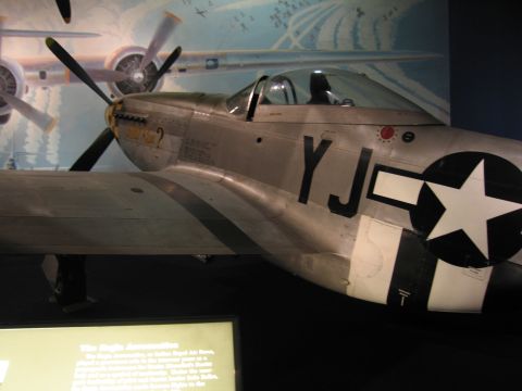 1991 Ford LTD Crown Victoria - bare-metal WWII fighter aircraft displayed in a museum, its fuselage marked with a white star-in-circle insignia and black 'YJ' codes.