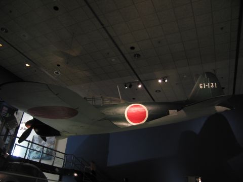 1991 Ford LTD Crown Victoria - green WWII aircraft suspended from a museum ceiling, bearing a large red disc roundel and the yellow tail code 61-131.
