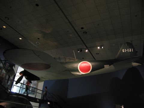 1991 Ford LTD Crown Victoria - green WWII aircraft with red disc roundels and tail code 61-131, hanging above a museum stairwell with visitors below.
