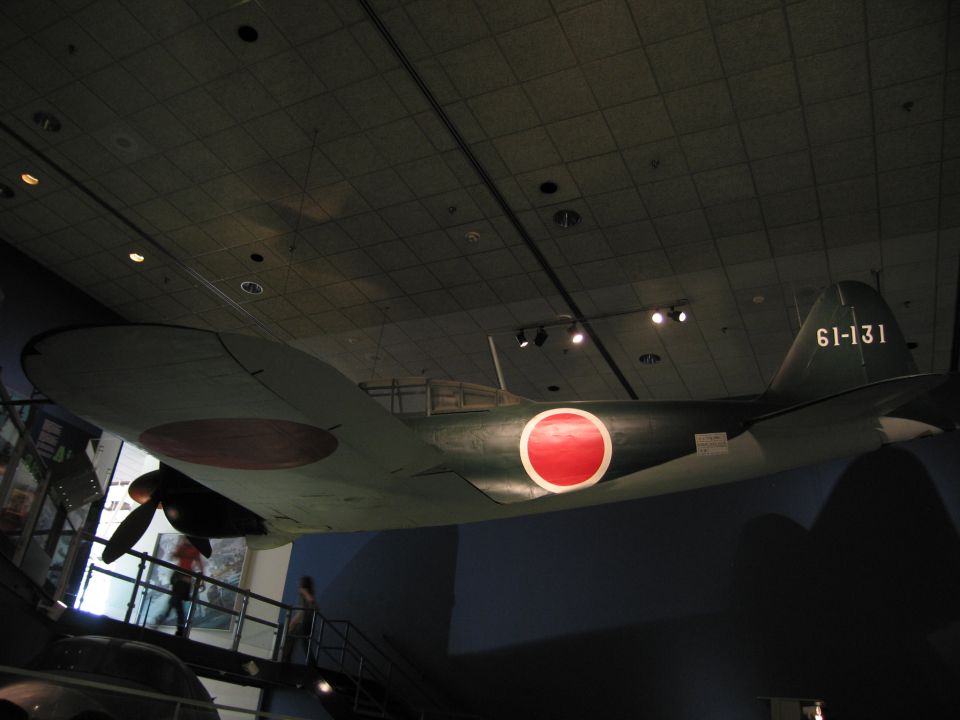 WWII aircraft with red roundels and code 61-131 suspended over a museum stairwell