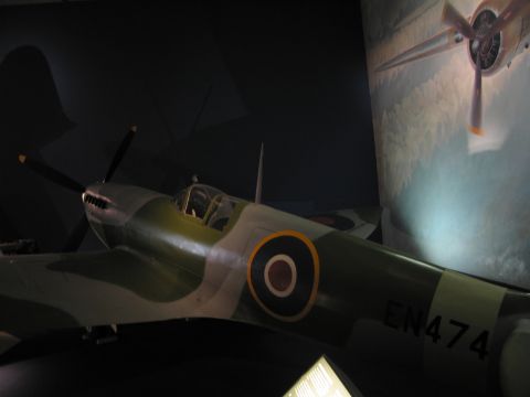 1991 Ford LTD Crown Victoria - camouflaged WWII fighter bearing an RAF roundel and the code EN474, displayed against a painted aircraft mural in a museum.