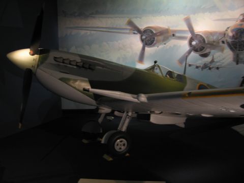 1991 Ford LTD Crown Victoria - green-and-silver WWII fighter aircraft with exposed landing gear, displayed before a mural of multi-engine bombers.