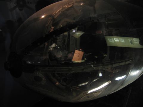1991 Ford LTD Crown Victoria - transparent bombardier nose section of a WWII aircraft, showing internal structure and a small placard, in a dark gallery.