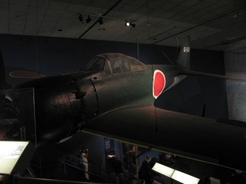 1991 Ford LTD Crown Victoria - dark green WWII single-engine fighter bearing a large red disc roundel, displayed above a museum balcony with visitors below.