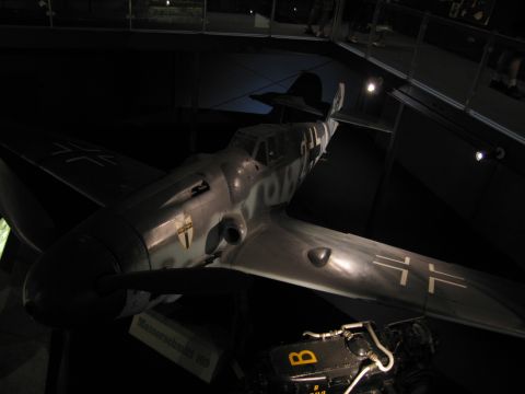 1991 Ford LTD Crown Victoria - grey WWII single-engine fighter with black cross markings on wing and fuselage, displayed in a dimly lit museum gallery.