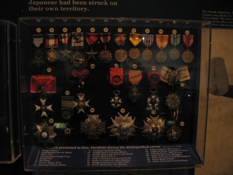 1991 Ford LTD Crown Victoria - lit glass display case holds rows of numbered military medals and ribbons beneath a wall placard describing a wartime career.