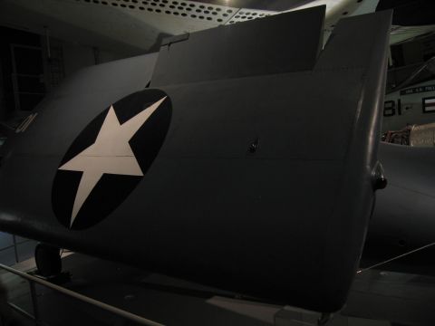 1991 Ford LTD Crown Victoria - folded gray military aircraft wing bearing a white star-in-circle insignia is displayed in a darkened museum.