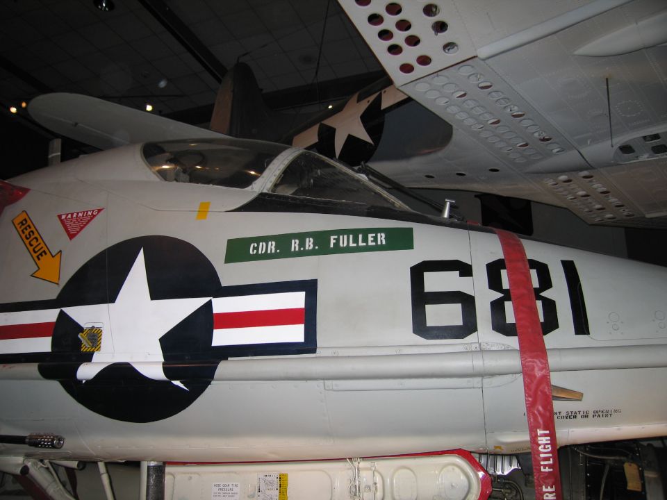 Side view of gray Navy jet 681 with star-and-bars insignia and folded wing