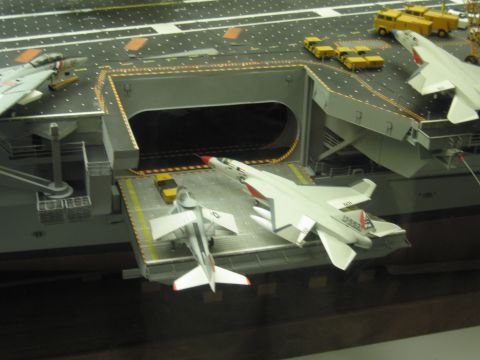 1991 Ford LTD Crown Victoria - model aircraft carrier's deck-edge elevator opening is surrounded by model jets and yellow tow vehicles.