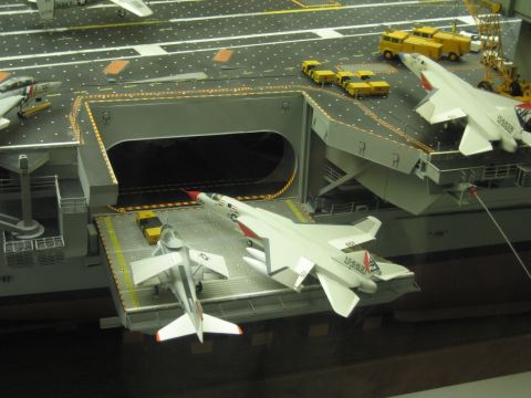 1991 Ford LTD Crown Victoria - model jet sits on a carrier deck elevator beside yellow flight-deck trucks and a crane on the scale model.