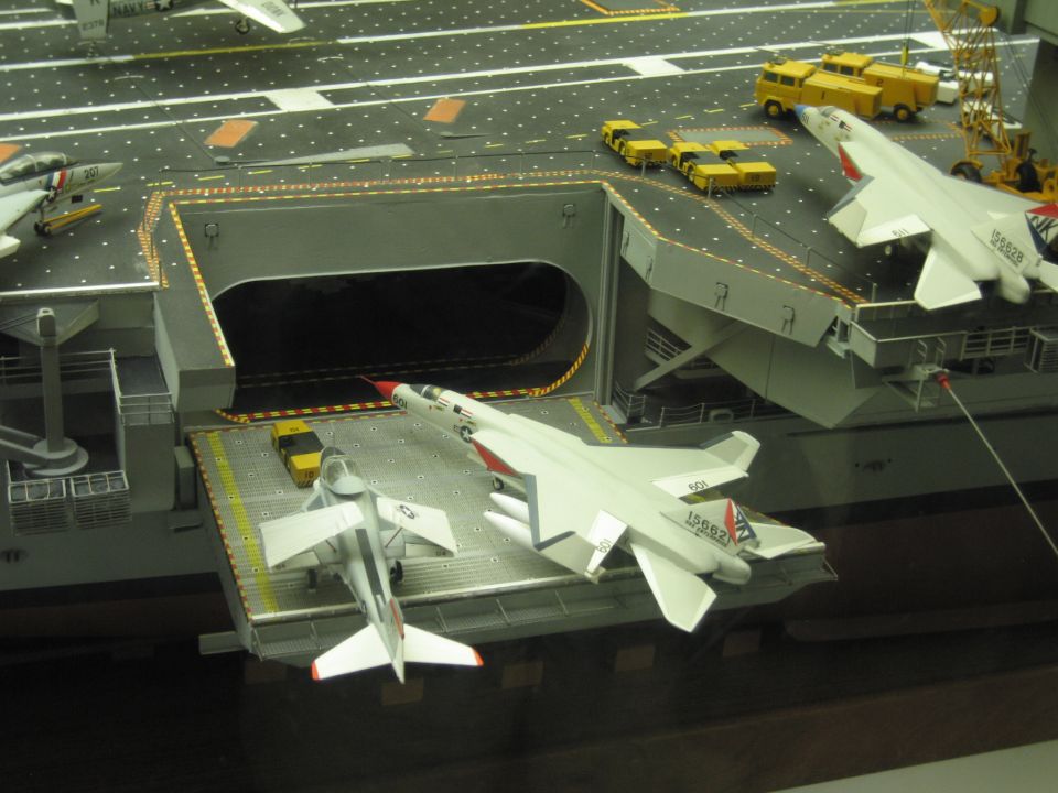 Aircraft carrier model deck elevator with a model jet and yellow flight-deck trucks