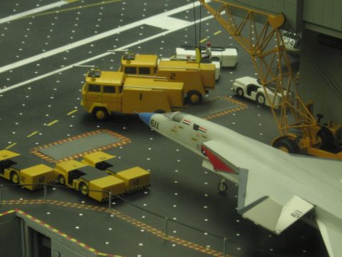 1991 Ford LTD Crown Victoria - Yellow model flight-deck fire trucks and tractors flank a white model jet numbered 611 on a carrier deck model.