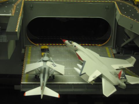 1991 Ford LTD Crown Victoria - top-down view of a carrier model's deck elevator shows two white model jets, one numbered 601, with folded wings.