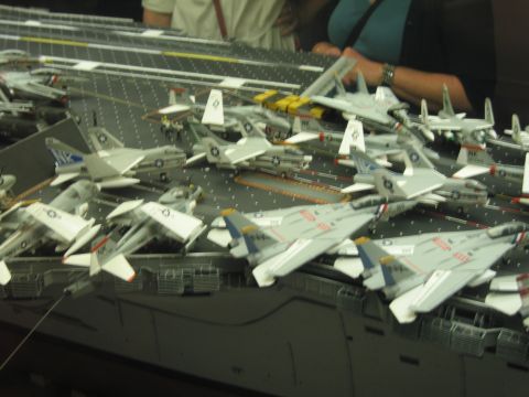 1991 Ford LTD Crown Victoria - detailed model aircraft carrier deck packed with gray Navy fighter jets, with museum visitors visible behind it.