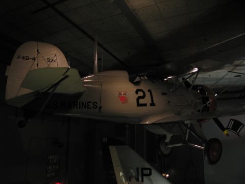 1991 Ford LTD Crown Victoria - vintage white biplane lettered U.S. MARINES and F4B-4 with the number 21, suspended in a dim museum hall.