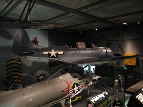 1991 Ford LTD Crown Victoria - gray WWII-era Navy aircraft marked 109 with a star insignia hangs in a museum above other displayed planes.