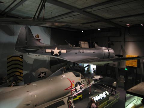 1991 Ford LTD Crown Victoria - gray Navy aircraft marked 109 with a white star insignia suspended above other display aircraft in a museum.