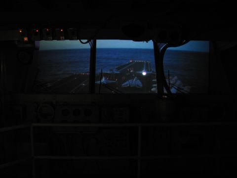 1991 Ford LTD Crown Victoria - View from a dark ship bridge with control panels, looking out the windows over the sea toward an illuminated deck.